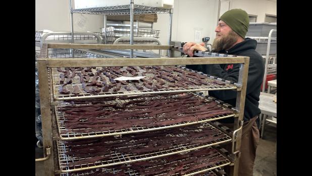 Josh Clark stands near a rack of drying venison jerky as he speaks with coworkers at Cutting Edge Meat Market in Piedmont, S.D. (Photo: Bart Pfankuch, South Dakota News Watch)